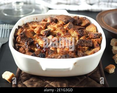 Bread pudding in white baking dish on brown heat pad with table set Stock Photo