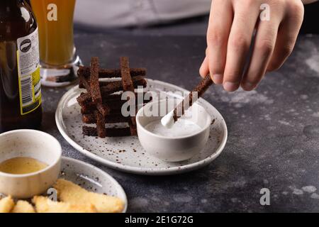 Delicious dark croutonsserved with aromatic garlic sauce. Man dips toast in sauce. Stock Photo