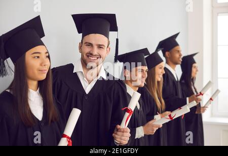 Student man with diploma in hands looking at camera standing next to his multiethnic classmates. Stock Photo