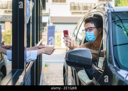 Asian man customer using mobile scan QR or NFC payment on smart phone paying for his coffee drink in coffee shop while he drive thru and Barista weari Stock Photo