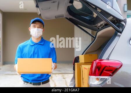 Asian Delivery man services courier working with cardboard boxes on van during the Coronavirus (COVID-19) pandemic, courier wearing medical mask and l Stock Photo