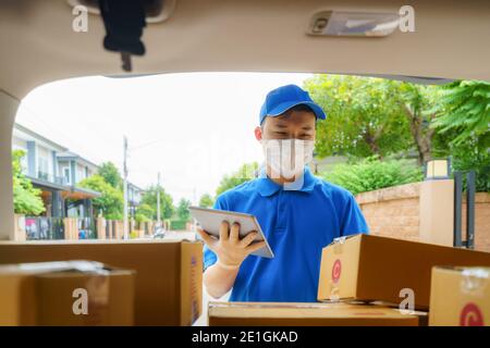 Asian Delivery man services courier working with cardboard boxes on van during the Coronavirus (COVID-19) pandemic, courier wearing medical mask and l Stock Photo