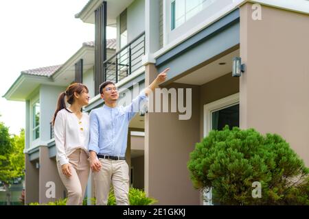 Portrait of Asian couple walking and hugging together looking happy in front of their new house to start new life. Family, age, home, real estate and Stock Photo