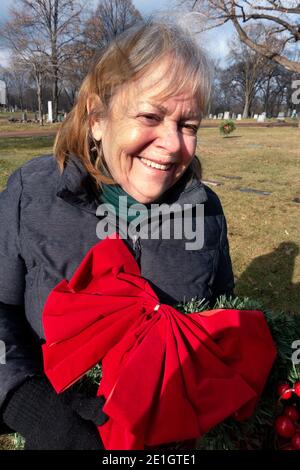 Woman holding a Christmas wreath with a red bow to decorate a cemetery grave and pay respects for her parents. Minneapolis Minnesota MN USA Stock Photo