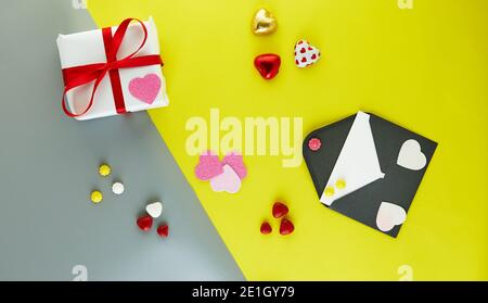 Valentine's Day card with candy hearts, gift and envelope for your wishes on yellow-gray background Stock Photo