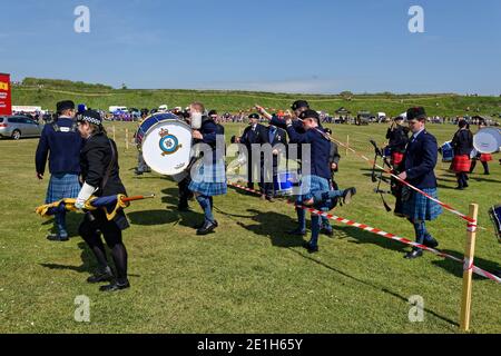 Members of a Marching Pipe band climbing over the temporary red and white tape barrier after their performance at an event in Arbroath. Stock Photo