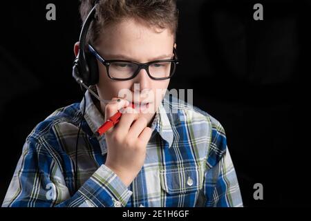 Boy with glasses and shirt and mouth mask with headset pen in mouth pondering Stock Photo
