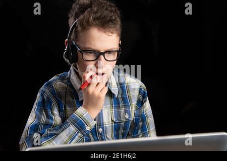 Boy with glasses and shirt and mouth mask with headset pen in mouth pondering Stock Photo
