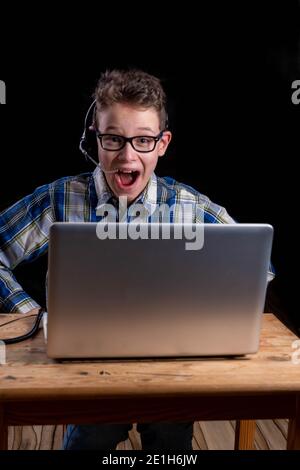 Boy with shirt and glasses joyfully using headset while e-learning on laptop Stock Photo