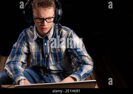 Boy with shirt and glasses doing homework on laptop with headset Stock Photo