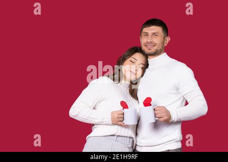 Newlyweds in love with white tea cups on a red background with side space. Spending time on St.Valentine's Day. Stock Photo
