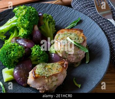 Pork tenderloin with herb butter and vegetables on a dark plate from above Stock Photo