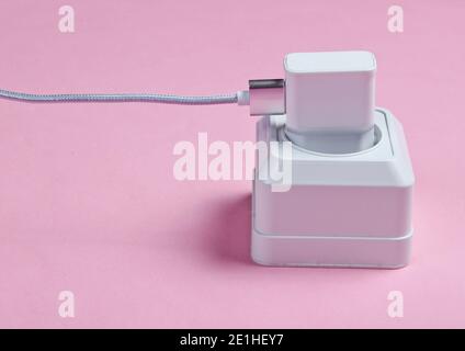 Charger plugged into power outlet on pink background Stock Photo