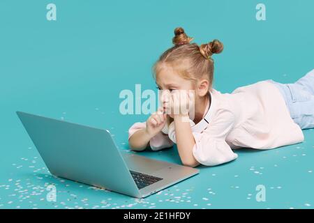 Smart child girl using laptop on cyan background. Education, online study, tv, distance learning. Primary school student during quarantine. Educationa Stock Photo