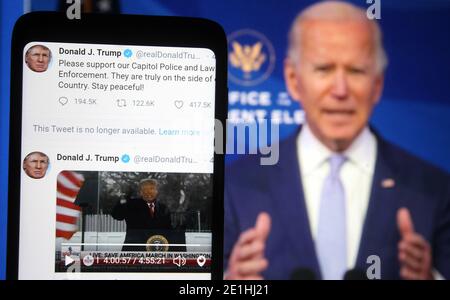 In this photo illustration, Donald Trump Twitter messages are seen displayed on a smartphone screen in front of a fragment of a video with U.S. President-elect Joe Biden addressing Trump supporters as they continue with protests in and near the U.S. Capitol in Washington during the U.S. Congress session to certify the 2020 Presidential election results. Stock Photo
