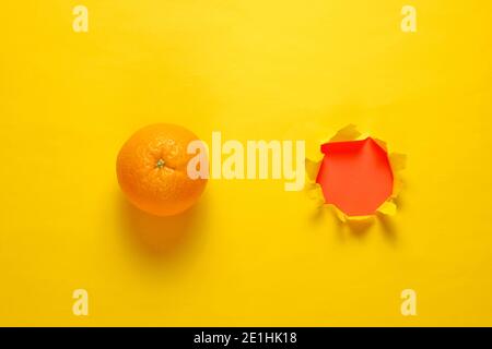 Orange and a torn hole in yellow paper. Minimalistic fruit concept Stock Photo