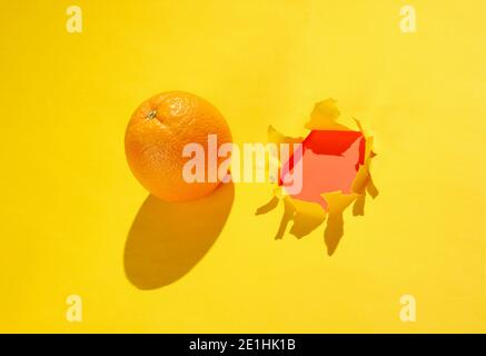 Orange and a torn hole in yellow paper. Minimalistic fruit concept Stock Photo