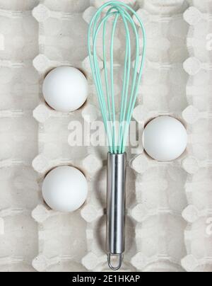 Whisk and eggs in tray. Top view, closeup Stock Photo