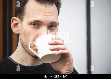 Portrait of a caucasian man drinking tea or coffee from a white mug Stock Photo