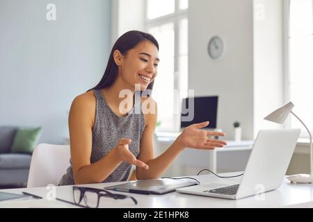 Happy young Asian woman sitting at desk at home and using laptop computer for video call Stock Photo