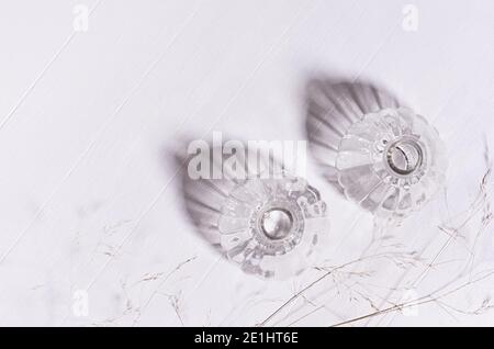 Elegant fracile lifestyle background with dry grass straws, transparent bottles in sunlight, shadows on white wood board, top view, border. Stock Photo