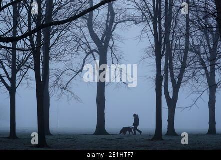 Leicester, Leicestershire, UK. 7th January 2021. UK weather. A man walks a dog across a foggy Victoria Park during the coronavirus third national lockdown. Credit Darren Staples/Alamy Live News. Stock Photo