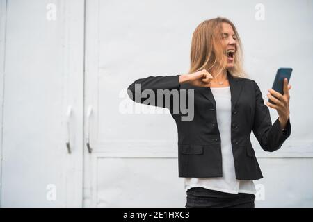 Outdoor portrait of ecstatic modern businesswoman who is joyful. She is holding smartphone. Stock Photo