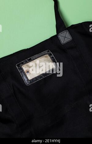 A black old bag with an aged label sewn onto the bag. Empty space. Vertical flat lay shot on a green background Stock Photo