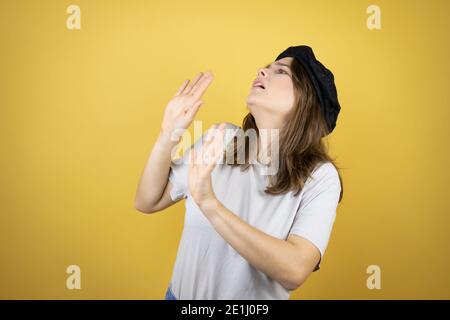 Beautiful young caucasian girl wearing french look with beret over isolated yellow background scared with her arms up like something falling from abov Stock Photo