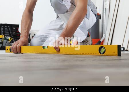 man worker hands installing timber laminate floor. Precise finishing using spirit level. Wooden floors house renovation. Stock Photo