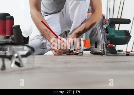 man worker hands installing timber laminate floor, takes measurement with the tape measure and pencil. Wooden floors house renovation. Stock Photo