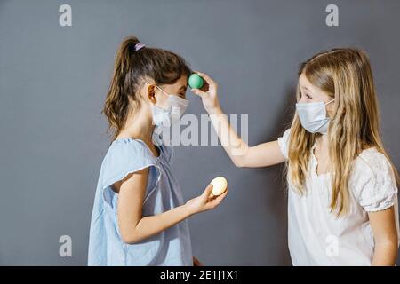 Easter celebration during Covid-19 concept. A funny portrait of two girls having fun on Easter wearing protective masks They are holding painted eggs Stock Photo