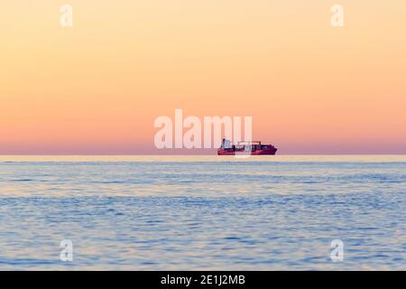 International Container Cargo ship on the open sea horizon at sunset. Water transport International.  Side view. Defocused photo with blur in motion. Stock Photo