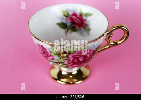 An antique teacup with pink roses and gold rim against a pink background. Stock Photo