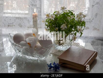 Spring flowers in a glass and white eggs in a crystal vase on a white background. Stock Photo