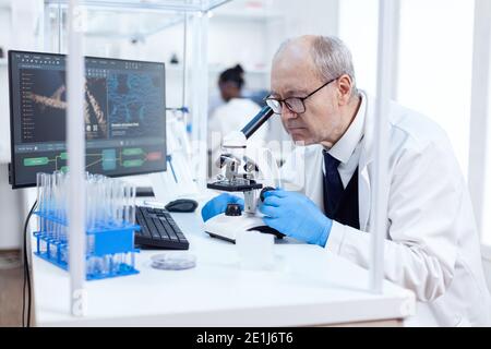 Senior scientist in chemistry laboratory uses microscope working on new medicine. Chemist researcher in sterile lab doing experiments for medical industry using modern technology. Stock Photo