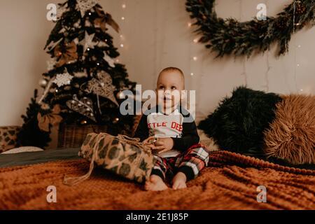 Baby girl sitting in pajamas on the bed in the bedroom and opens a gift. Christmas morning. New Year's interior. Valentine's Day celebration Stock Photo
