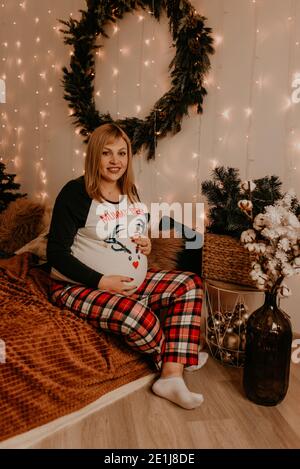 pregnant woman sits in pajamas with on the bed in the bedroom. Christmas morning. New Year's interior. Valentine's Day celebration Stock Photo