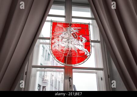 Vilnius, Lithuania - November 9, 2019: Decorational coat of arms of Lithuania made of stained glass hanging on the window between curtains. Stock Photo