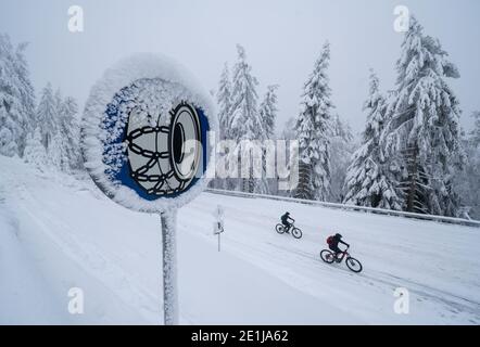 Schmitten, Germany. 07th Jan, 2021. A sign on the road to the summit plateau of the Großer Feldberg warns drivers to put on their snow chains, while two mountain bikers ride uphill over an icy road on the right. The access road to the snow-covered, highest elevation of the Taunus is still closed to road traffic. Credit: Frank Rumpenhorst/dpa/Alamy Live News Stock Photo