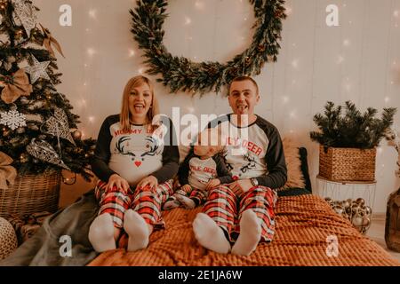 cheerful happy family in pajamas with child sitting on bed in bedroom. parents show tongues. new year family clothes looks outfits. Valentine's Day Ce Stock Photo