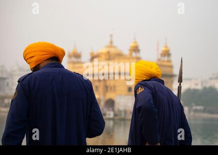(Selective focus) Two security guards, wearing the Dastar, are walking in front of the  Golden Temple during the covid-19 pandemic. Amritsar, India. Stock Photo
