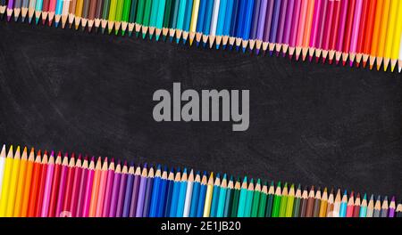 Border of colorful wooden pencils in leaning row on a blank blackboard, back to school concept.