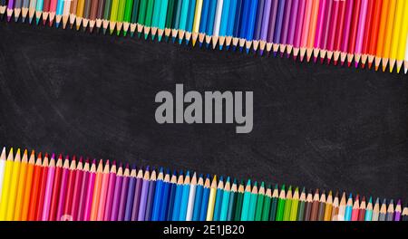 Border of colorful wooden pencils in leaning row on a blank blackboard, back to school concept. Stock Photo