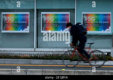 A man wearing a protective mask rides his bike past an advertisement on a department store.As Coronavirus  (Covid-19) infections surge, Japanese authorities have declared a State of emergency in Tokyo and three neighboring prefectures. Stock Photo