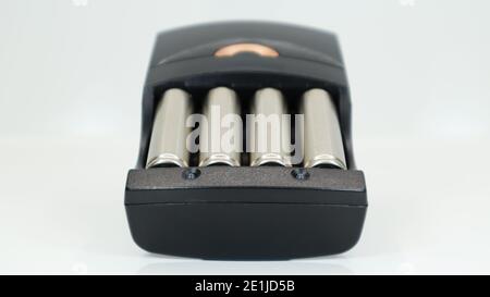 Rechargeable alkaline batteries in a battery charger on a white background. AA fast charger in black. The battery is charging Stock Photo