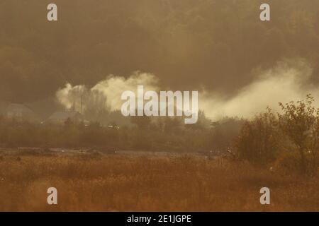 Landscape in Romania's countryside. Smoke coming out from a field beside the houses. Stock Photo