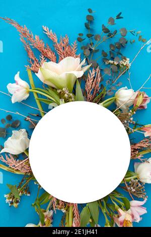 From above of bouquet of various plants and flowers arranged on vivid blue background with white blank circle in studio Stock Photo