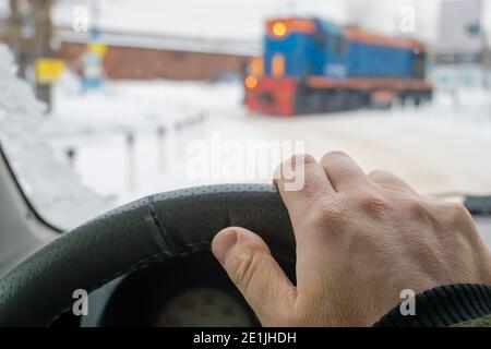 the driver's hand on the steering wheel of a car that has stopped, waits and passes the locomotive of the train that blocked the road Stock Photo