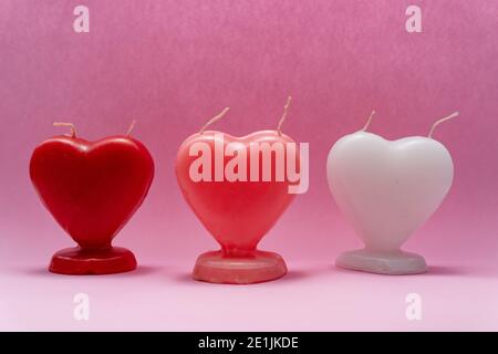 3 unlit heart-shaped candles in 3 different colors, on a pink background, for valentine's Day, Love and Friendship Day Stock Photo